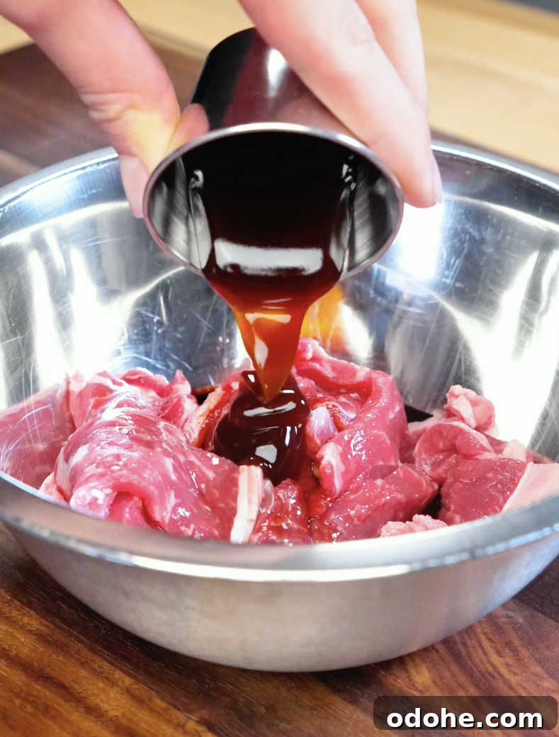 Dark soy sauce marinade being poured over thinly sliced strip steak with lemongrass and garlic to prepare flavorful Vietnamese-style Lemongrass Beef.