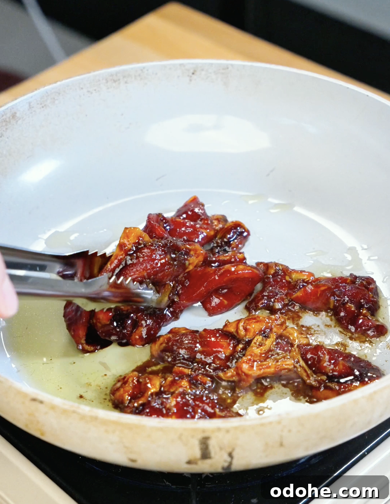 Tongs tossing thinly sliced beef coated in a sticky lemongrass garlic marinade while cooking in a skillet for this savory homemade Lemongrass Beef Recipe.