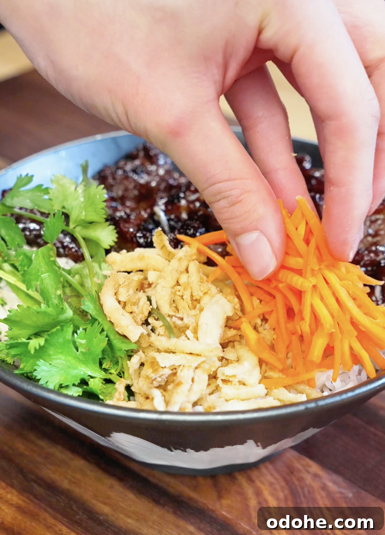 Fresh shredded carrots being added to a lemongrass beef rice bowl with cilantro and crispy onions for extra texture and vibrant flavor.