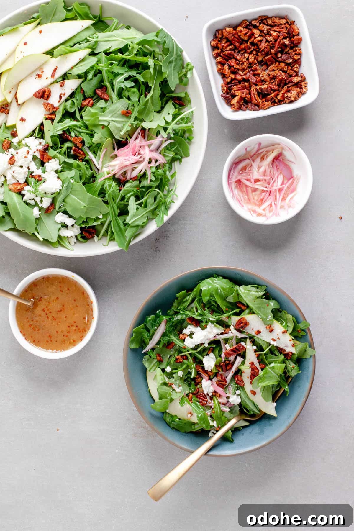 An arugula pear salad in a large bowl with a serving in a smaller blue bowl, topped with goat cheese and shallots.