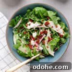 A small bowl of pear arugula salad topped with goat cheese and spiced pecans.