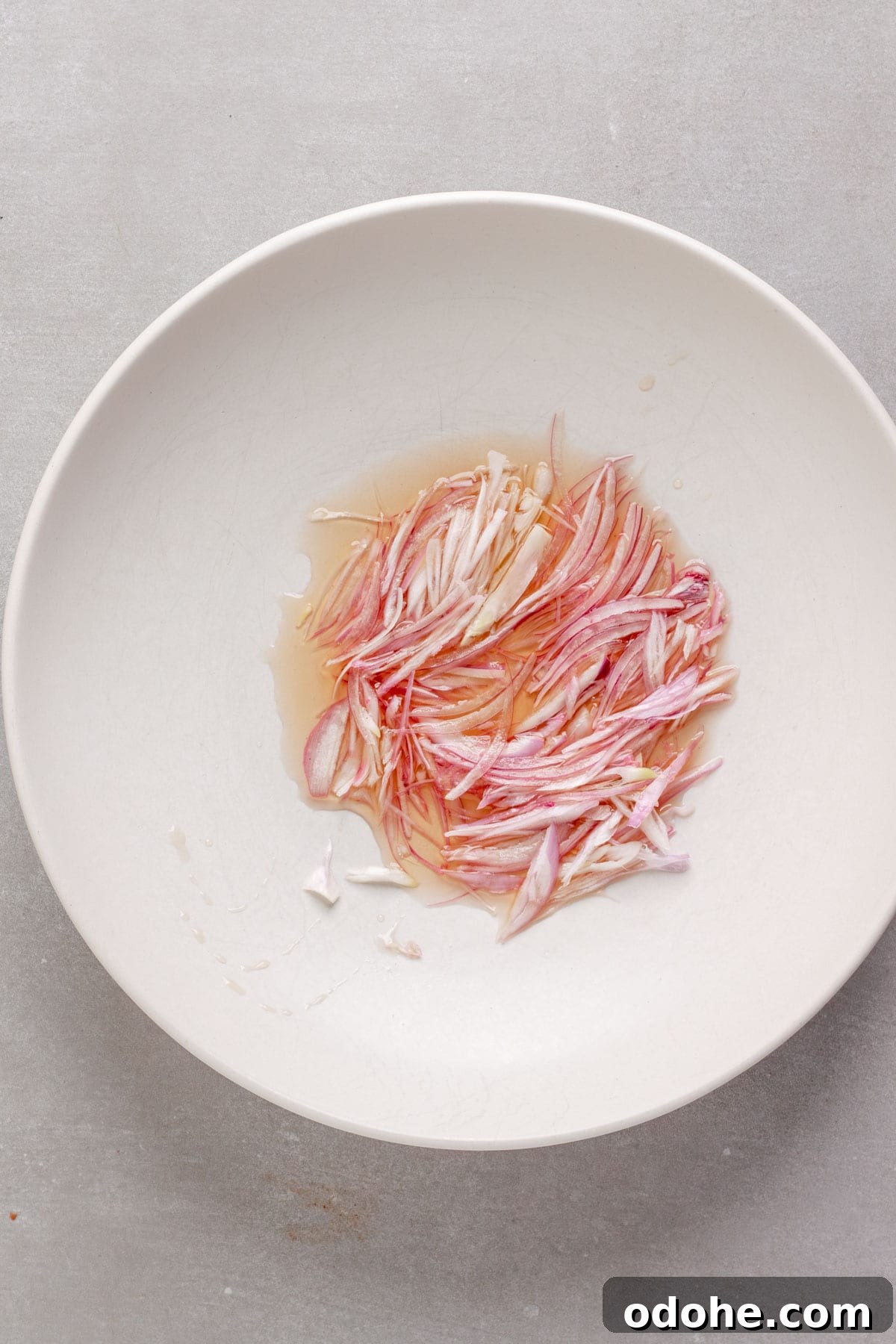 Thinly sliced shallots soaking in white balsamic vinegar in a medium bowl.
