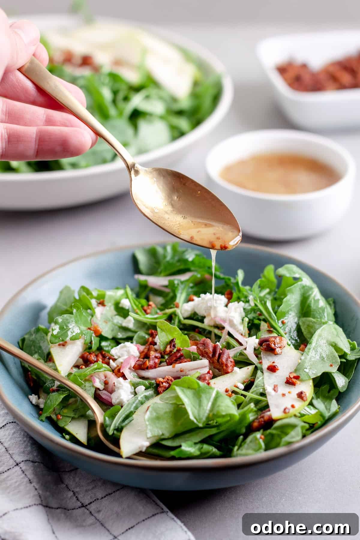 A spoonful of white balsamic vinaigrette drizzling onto a salad of arugula and pears.