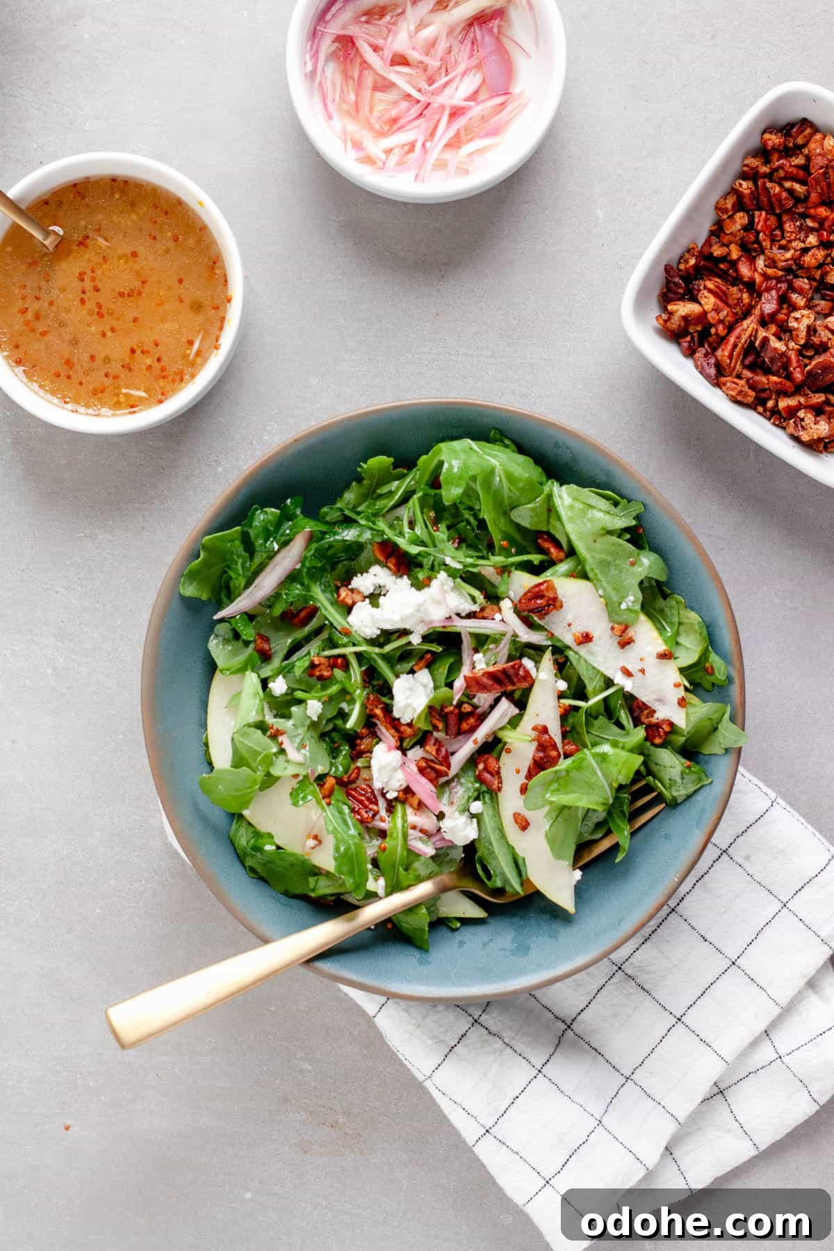 A small bowl of pear arugula salad topped with goat cheese and spiced pecans.