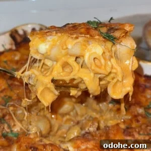A close-up of a cheesy baked macaroni and cheese being lifted from a casserole dish, with melted cheese stretching and garnished with fresh herbs.