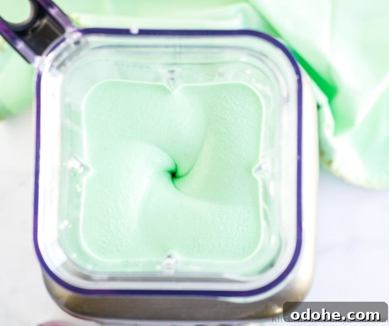 Vanilla ice cream, milk, food coloring, and mint are combined together in a blender.