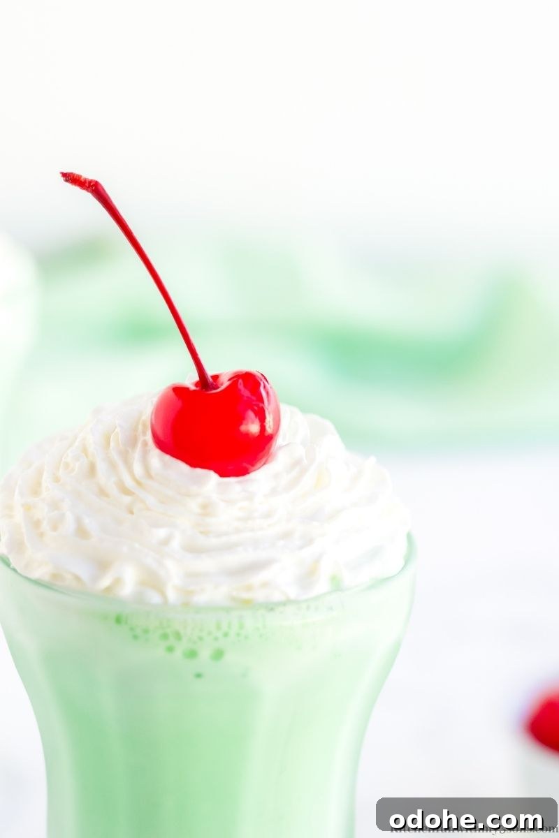 A homemade Shamrock Shake in a milkshake glass, topped with whipped cream and a cherry.