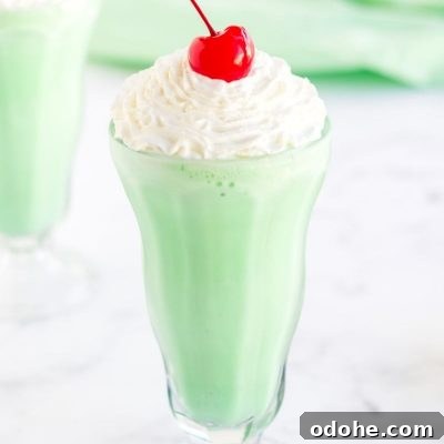 A homemade Shamrock Shake in a milkshake glass, topped with whipped cream and a cherry.