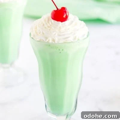 A homemade Shamrock Shake in a milkshake glass, topped with whipped cream and a cherry.