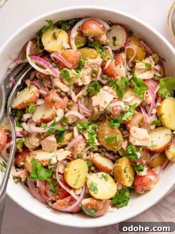 potato and tuna salad in white bowl with serving spoons.