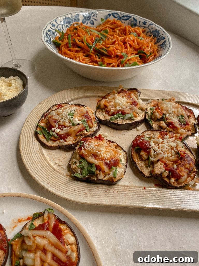 eggplant pizzas on a dish with a bowl of spaghetti and small bowl of parmesan