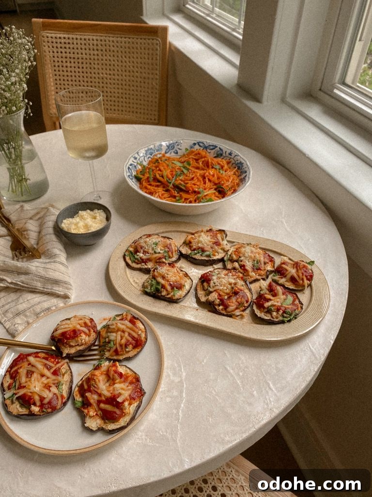 eggplant pizzas on a dish with a bowl of spaghetti and small bowl of parmesan and glass of white wine on a table