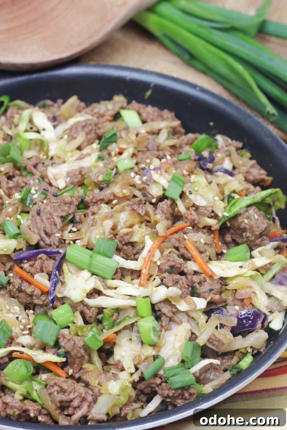 Gluten-Free Inside-Out Egg Roll Recipe: Crispy, Flavorful Wraps 2 Inside out egg roll in a skillet with green onions on top and a wooden spoon and white plates behind it.