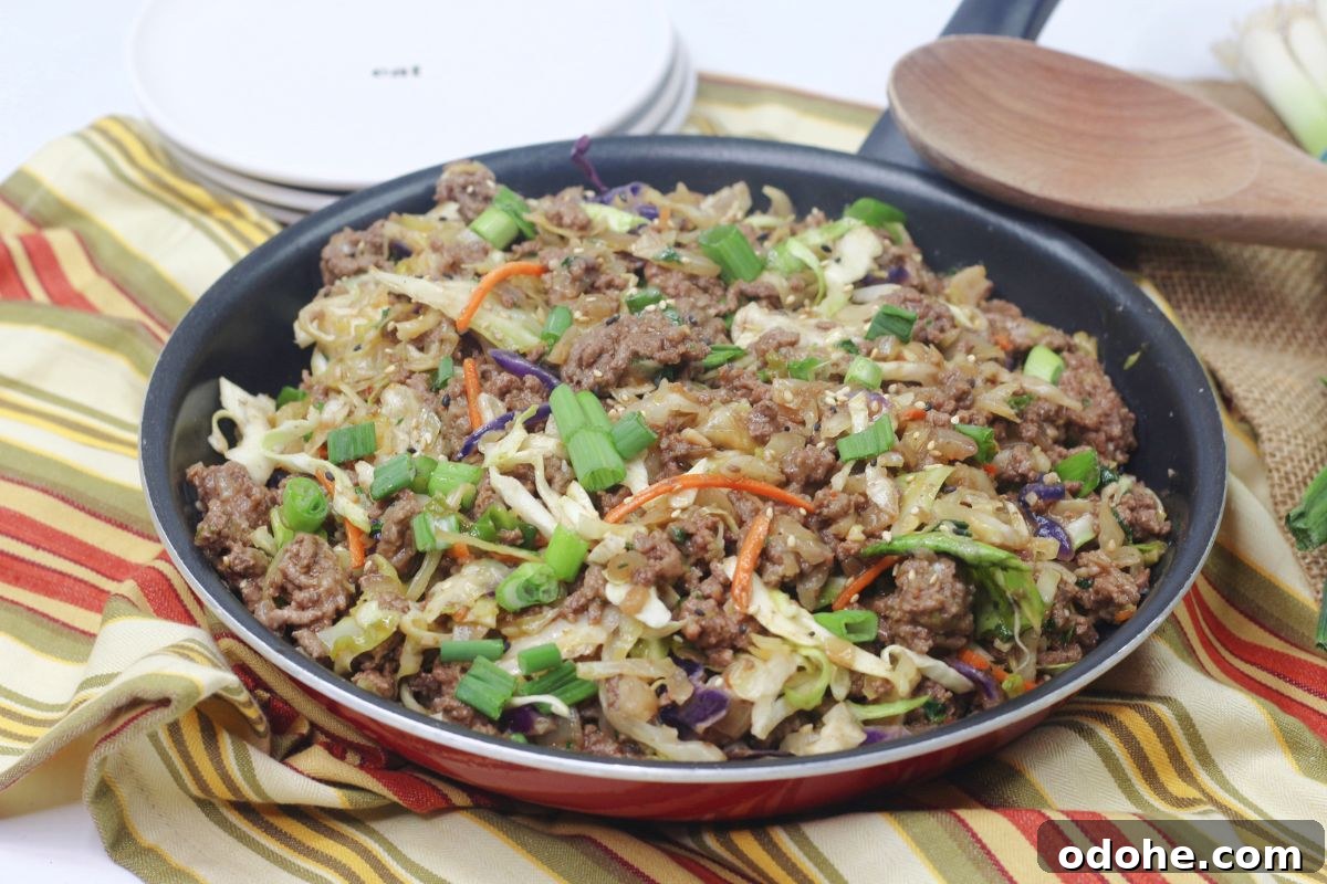Gluten-Free Inside-Out Egg Roll Recipe: Crispy, Flavorful Wraps 13 Inside out egg roll in a skillet with green onions on top and a wooden spoon and white plates behind it.