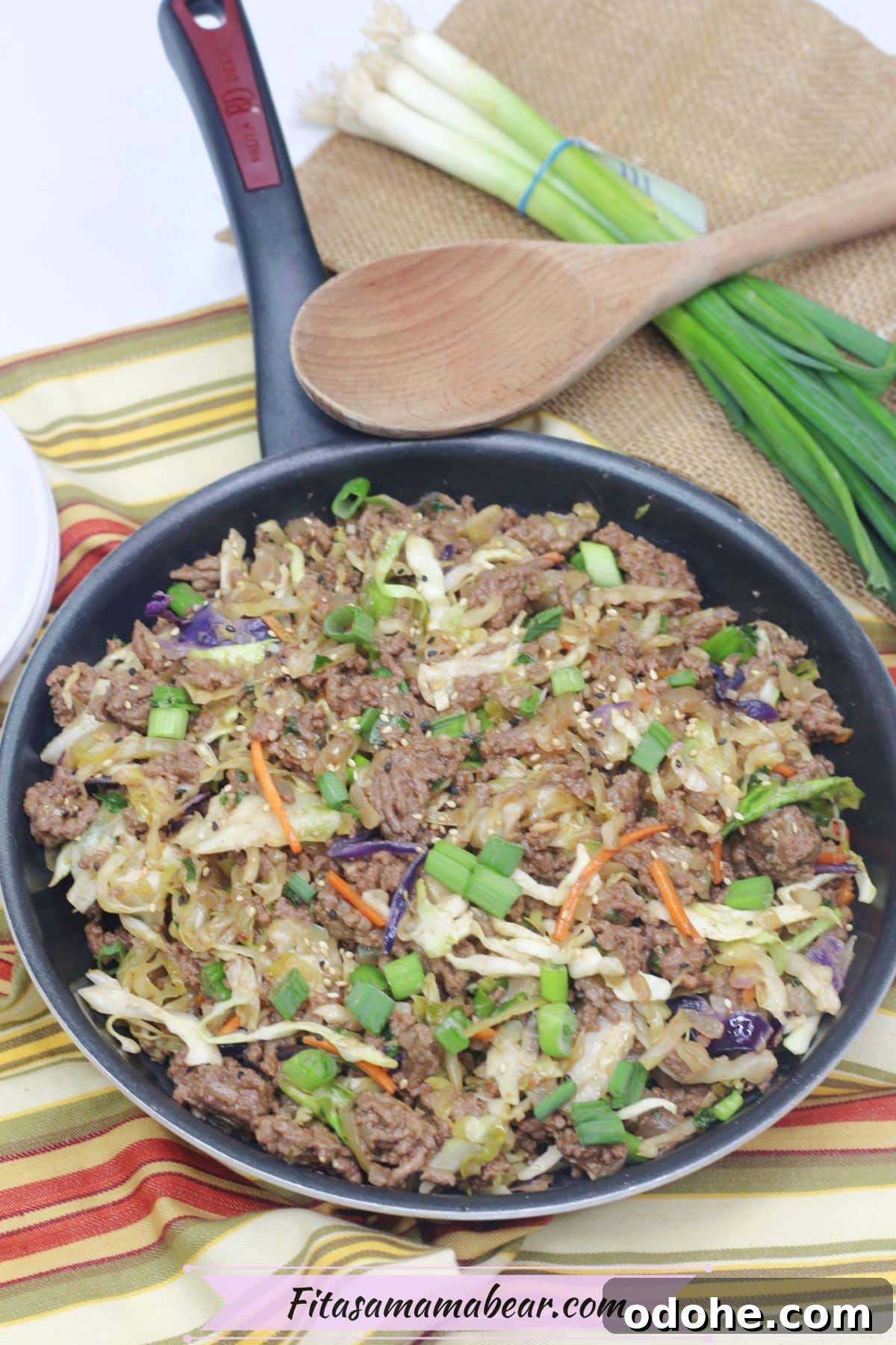 Gluten-Free Inside-Out Egg Roll Recipe: Crispy, Flavorful Wraps 7 Inside out egg roll in a skillet with green onions on top and a wooden spoon and white plates behind it.