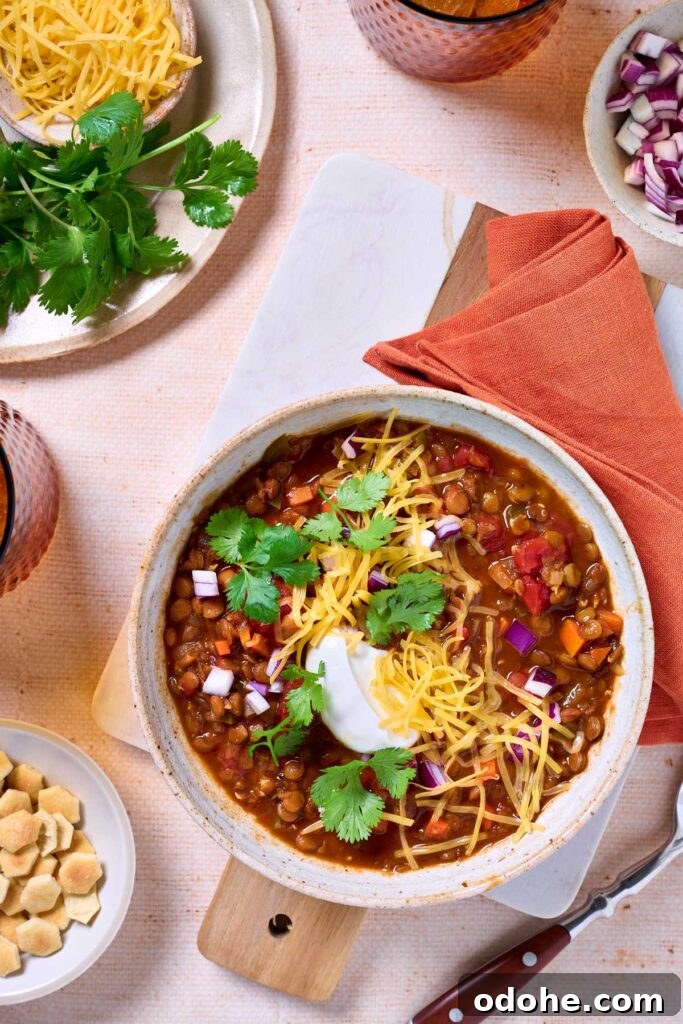 Cincinnati-Style Lentil Chili Recipe for Rich, Hearty Flavor 12 A bowl of lentil chili with veggies topped with shredded cheddar cheese, cilantro, chopped red onion and sour cream