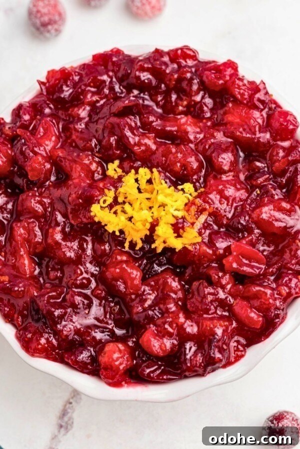 Bright red cranberry sauce in a white bowl, topped with orange zest as a garnish.