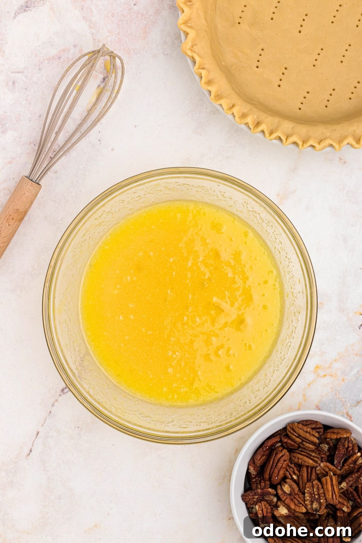 Eggs, sugar, and other pecan pie filling ingredients mixed together in a clear glass bowl.