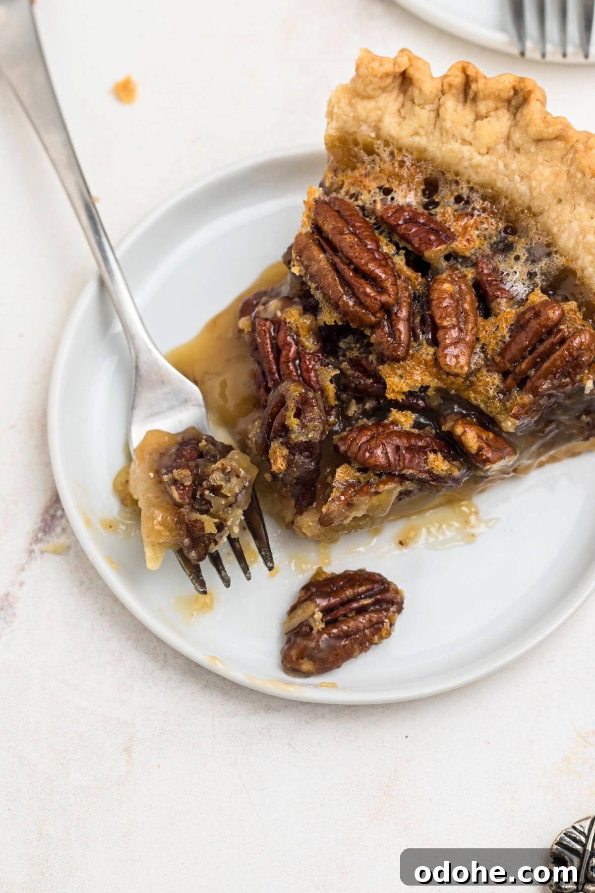 Pecan pie slice on a small white plate with a fork bite shot on the plate.