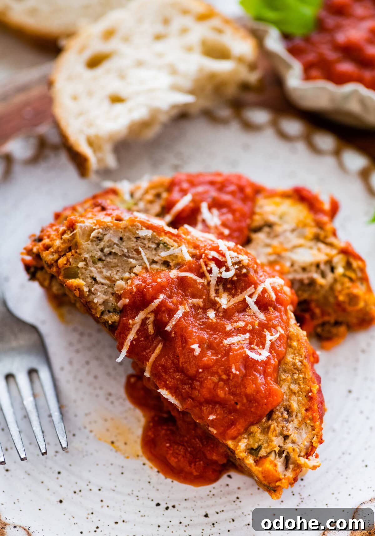 two slices of Italian meatloaf on a plate with extra sauce on top and bread on the side.