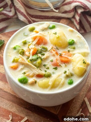 White bowl of chicken gnocchi soup on wood cutting board.
