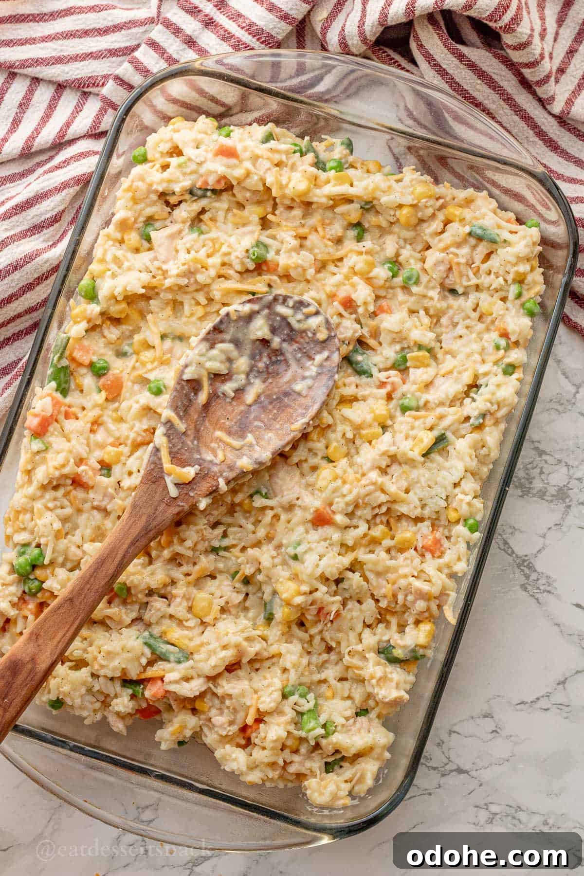 Cheesy Chicken, Rice & Veggie Casserole Recipe 9 Spreading unbaked chicken and veggies and rice in glass pan with wooden spoon.