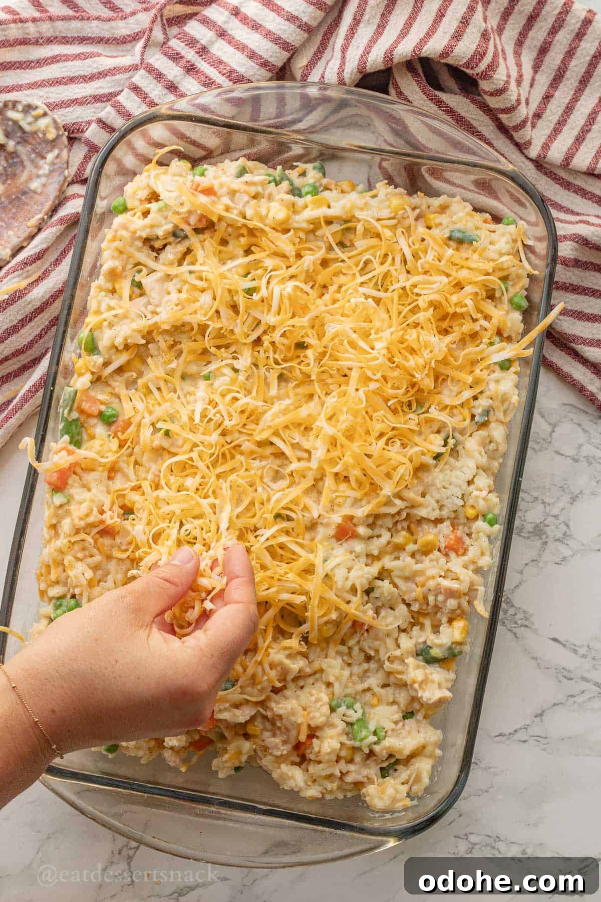 Cheesy Chicken, Rice & Veggie Casserole Recipe 10 Sprinkling cheese over raw chicken and rice in glass pan.