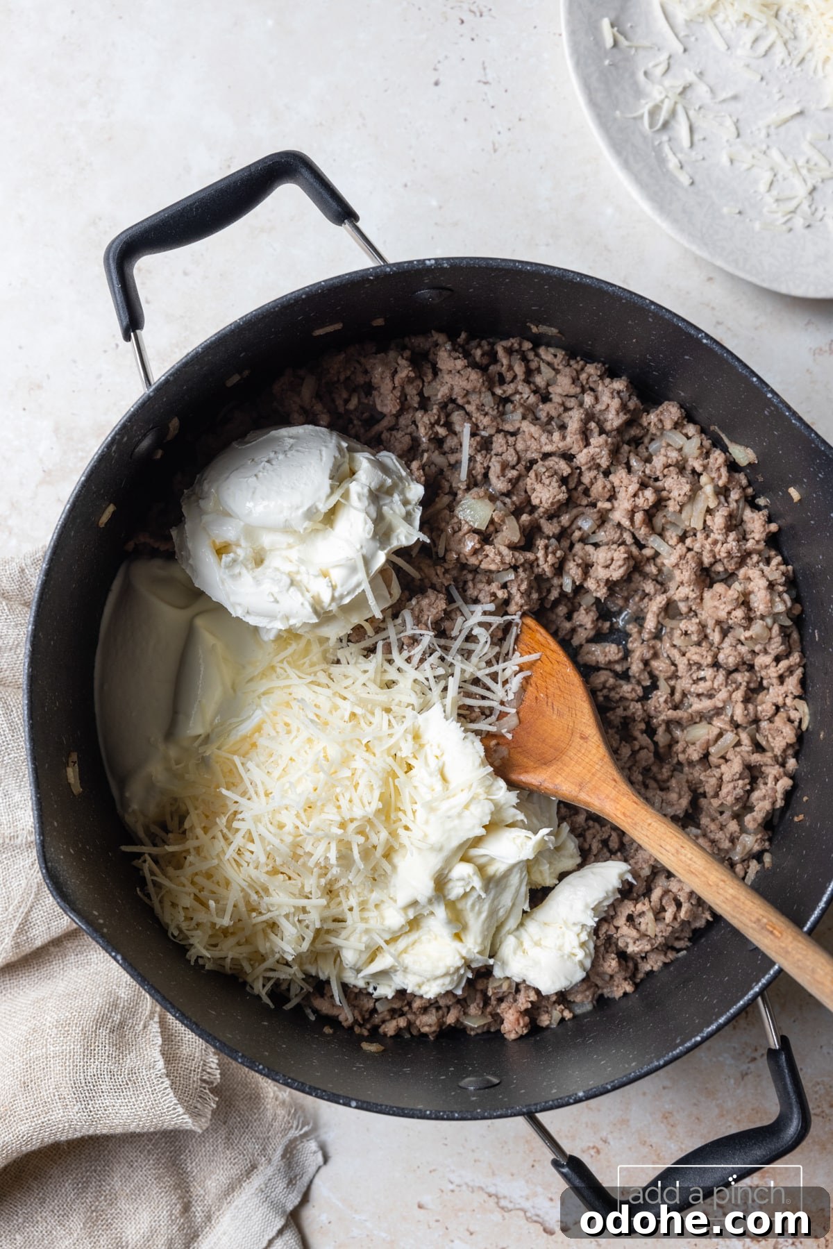 Photo of cooked ground beef with cheeses and sour cream in skillet.