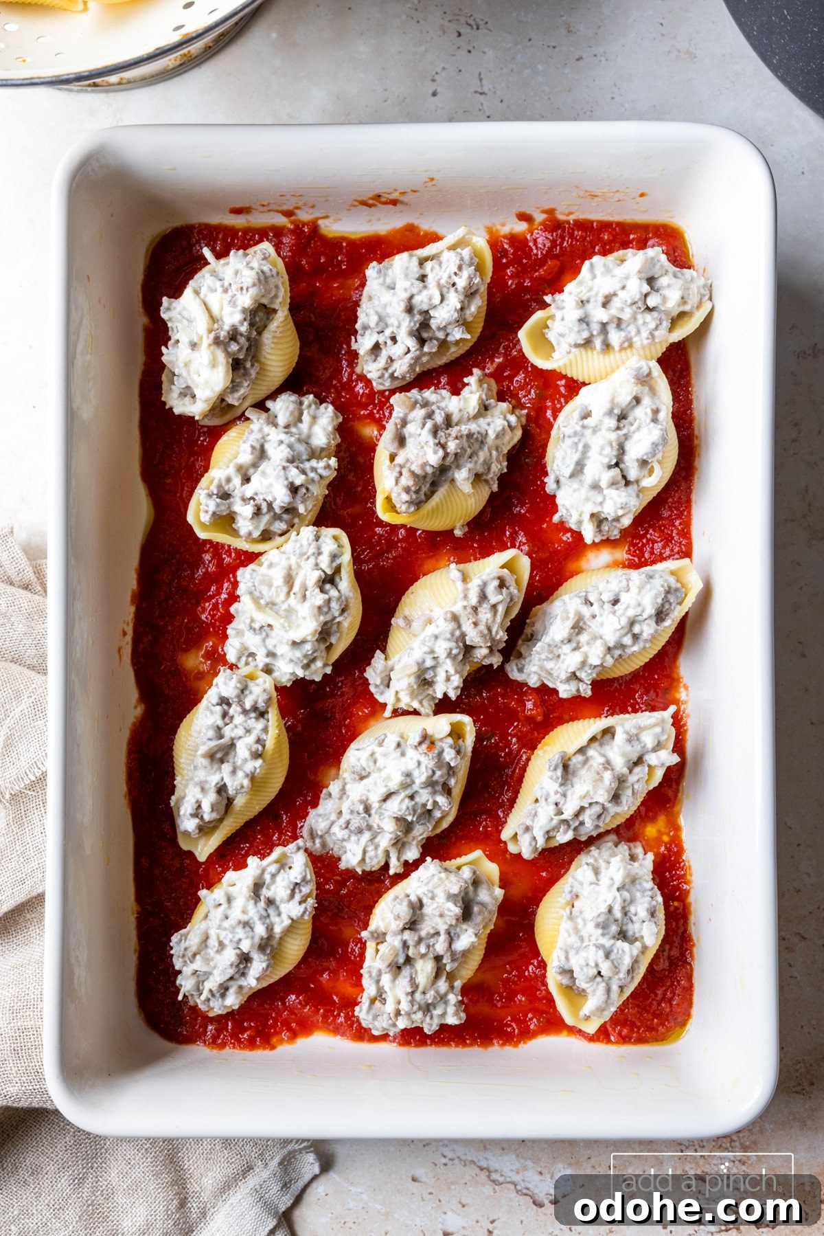 Photo of stuffed shells on tomato sauce in baking dish.