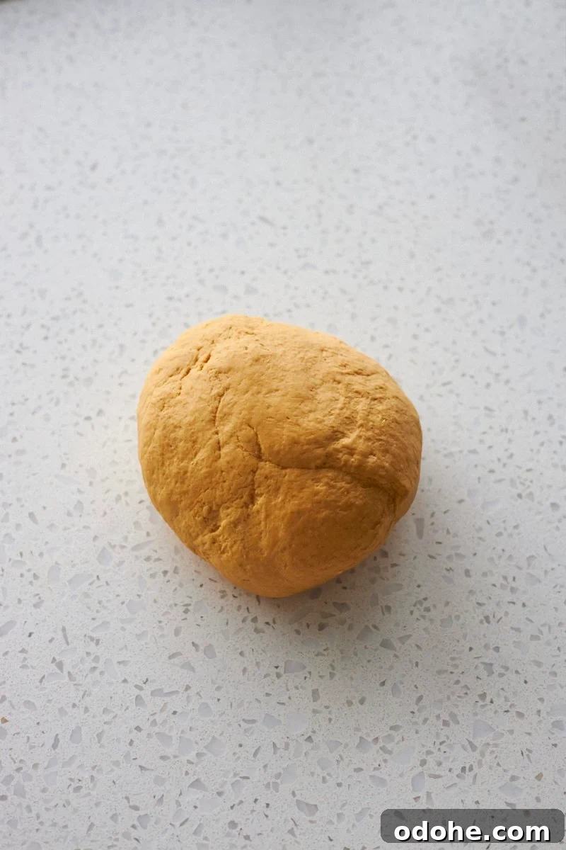 Pumpkin Sourdough Dinner Rolls Made with Discard 6 Kneaded dough on a work surface.