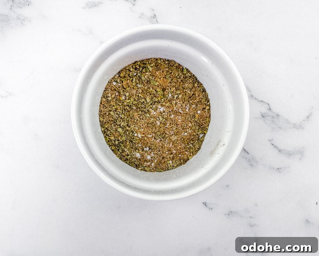 Slow Cooker Pork Chile Verde Recipe for Tender, Flavorful Pork 6 Overhead shot of a white bowl containing a mixture of dried herbs and spices, resting on a white marble surface with gray veins.