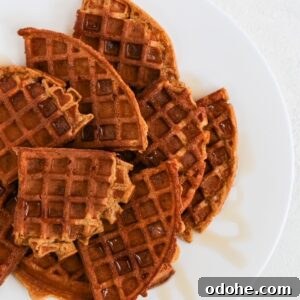 Quarters of round pumpkin waffles overlapping and topped with a drizzle of maple syrup on a white plate.