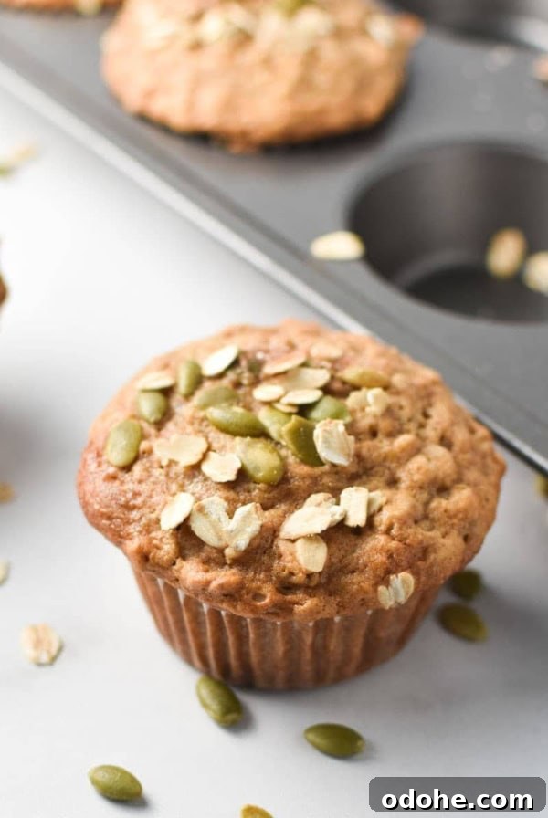 Cinnamon oatmeal muffins on a white table and in a baking pan, topped with oats and pumpkin seeds
