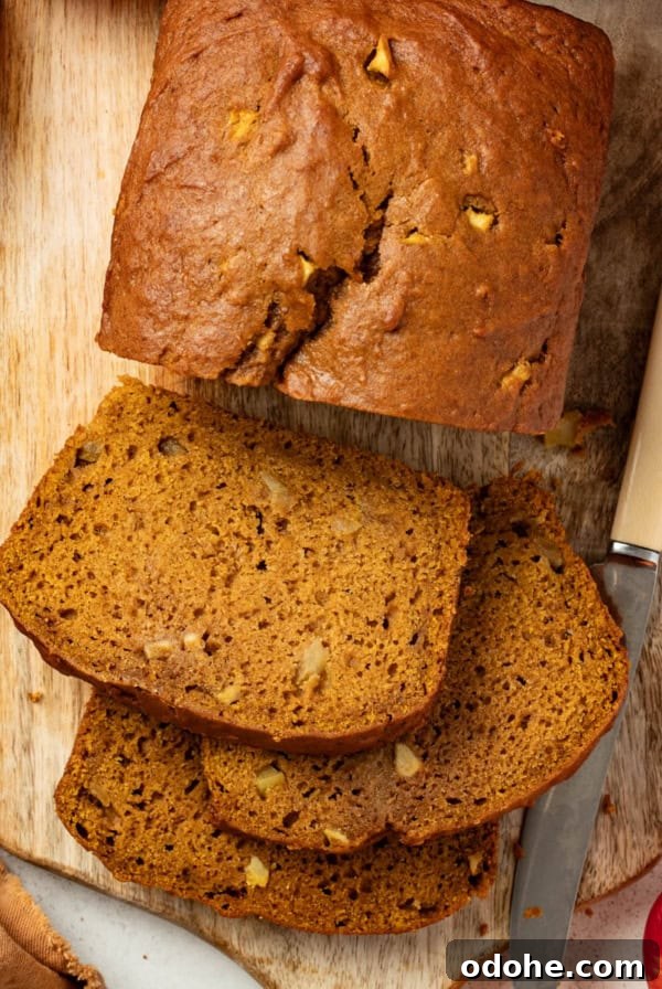 Slices of apple pumpkin bread on a serving platter next to a large loaf of the bread in the background.