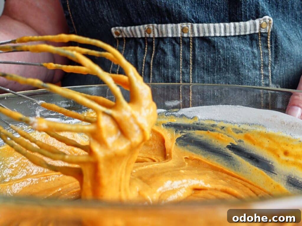 whisking pumpkin cake batter in large glass bowl.