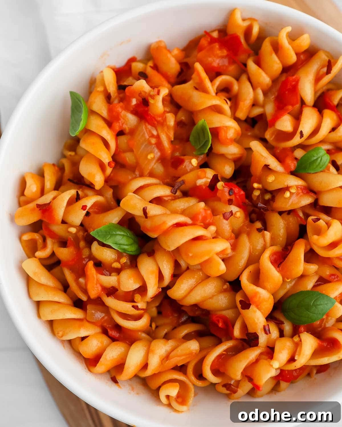 A close up image of fusilli in a red sauce with fresh basil and crushed red pepper.