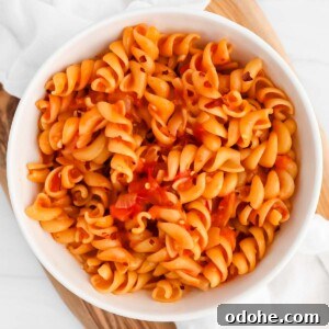 Pasta with red sauce and crushed red pepper flakes in a white bowl.