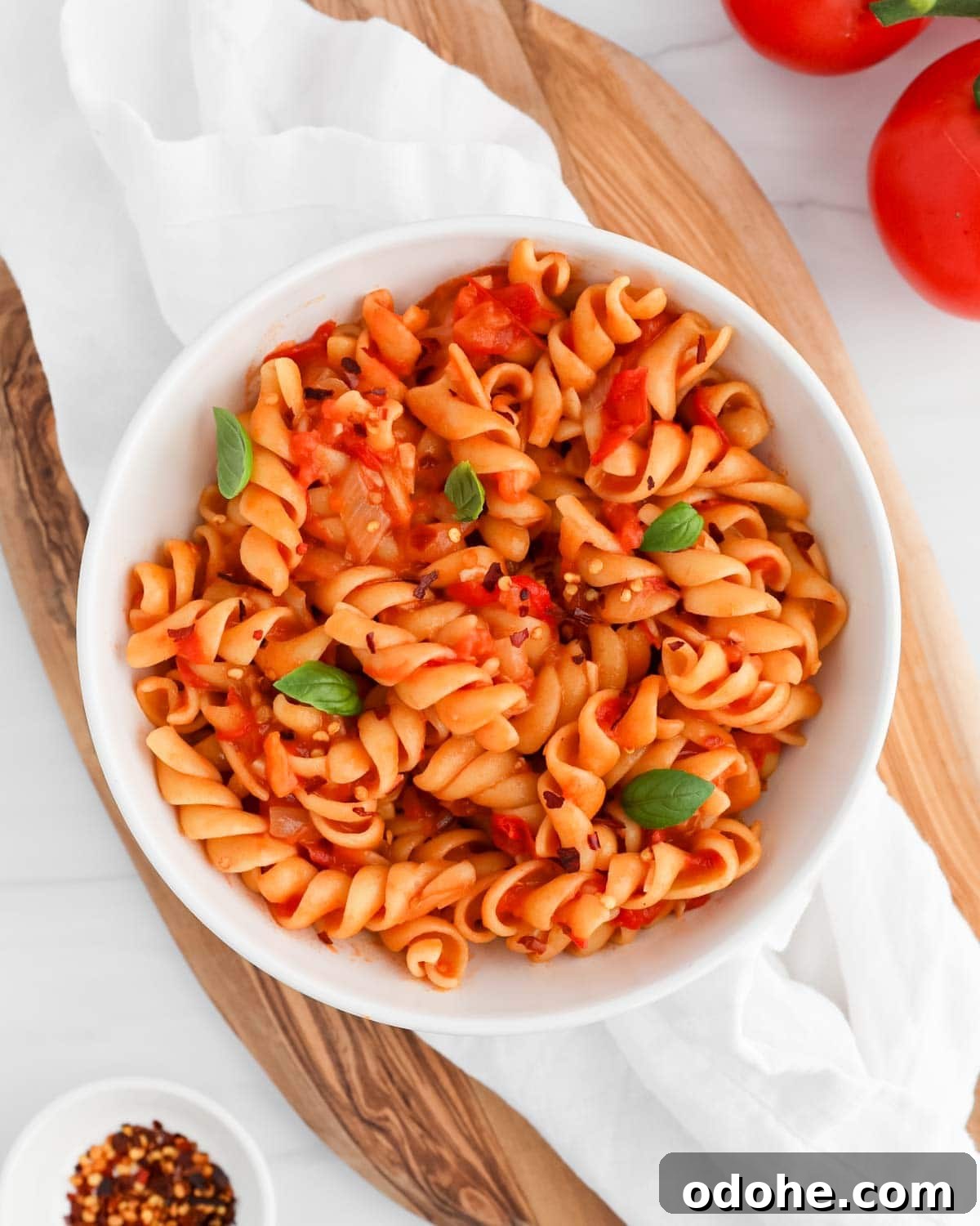 Pasta with red sauce, basil leaves, and crushed red pepper in a white bowl.