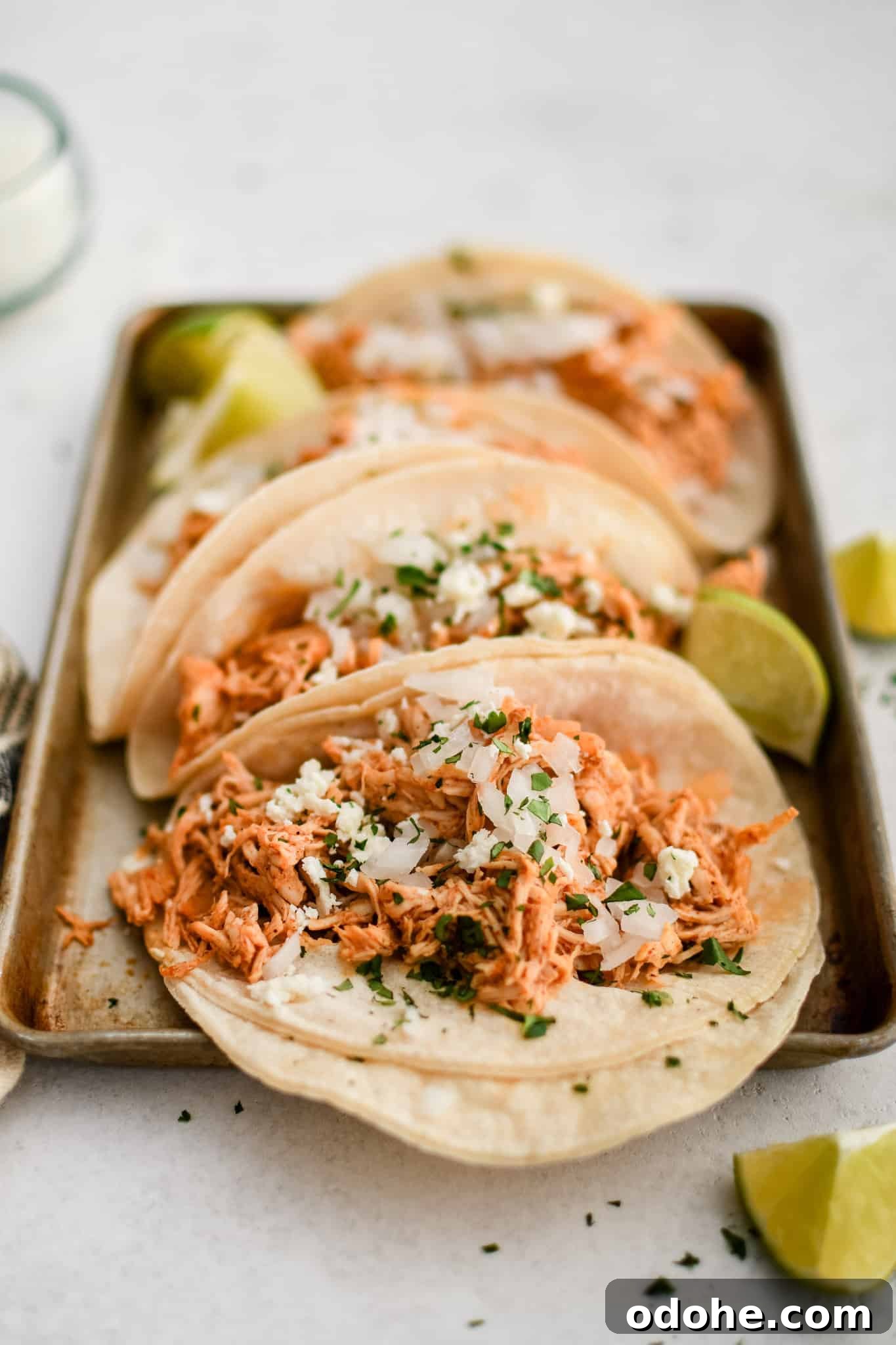 40+ Authentic Mexican Recipes for an Unforgettable Cinco de Mayo 15 Small baking sheet with four shredded chicken tacos topped with minced white onion and cilantro and served with fresh lime wedges.