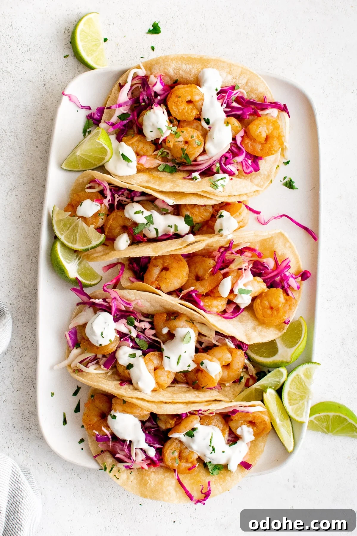 40+ Authentic Mexican Recipes for an Unforgettable Cinco de Mayo 17 Large white rectangle plate topped with five assembled shrimp tacos filled with cabbage slow, shrimp, and creamy taco sauce.