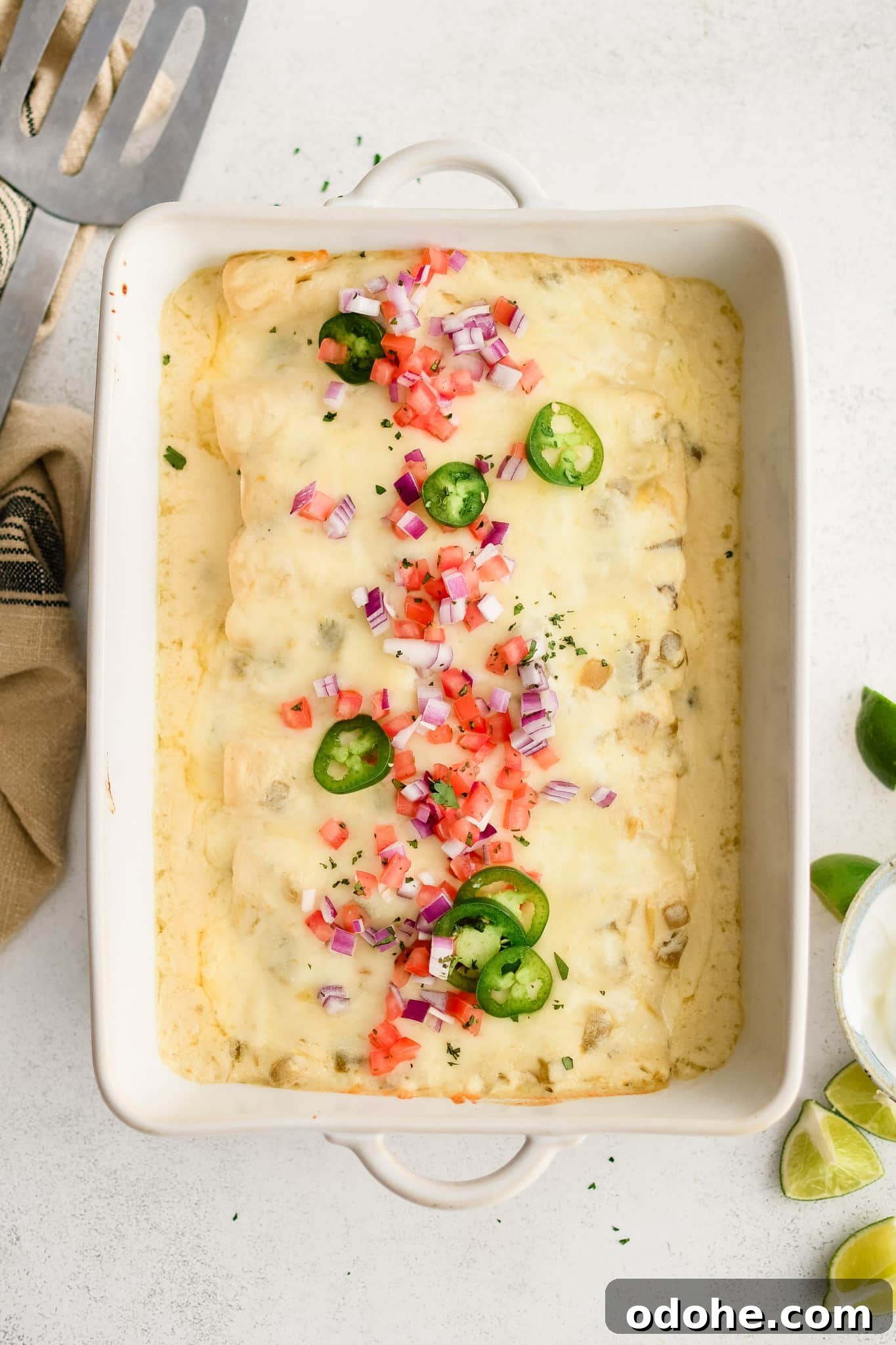 40+ Authentic Mexican Recipes for an Unforgettable Cinco de Mayo 19 Large white casserole baking dish filled with sour cream enchiladas smothered in a creamy sour cream and cheese sauce and topped with diced red onion, diced tomatoes, and sliced jalapenos.