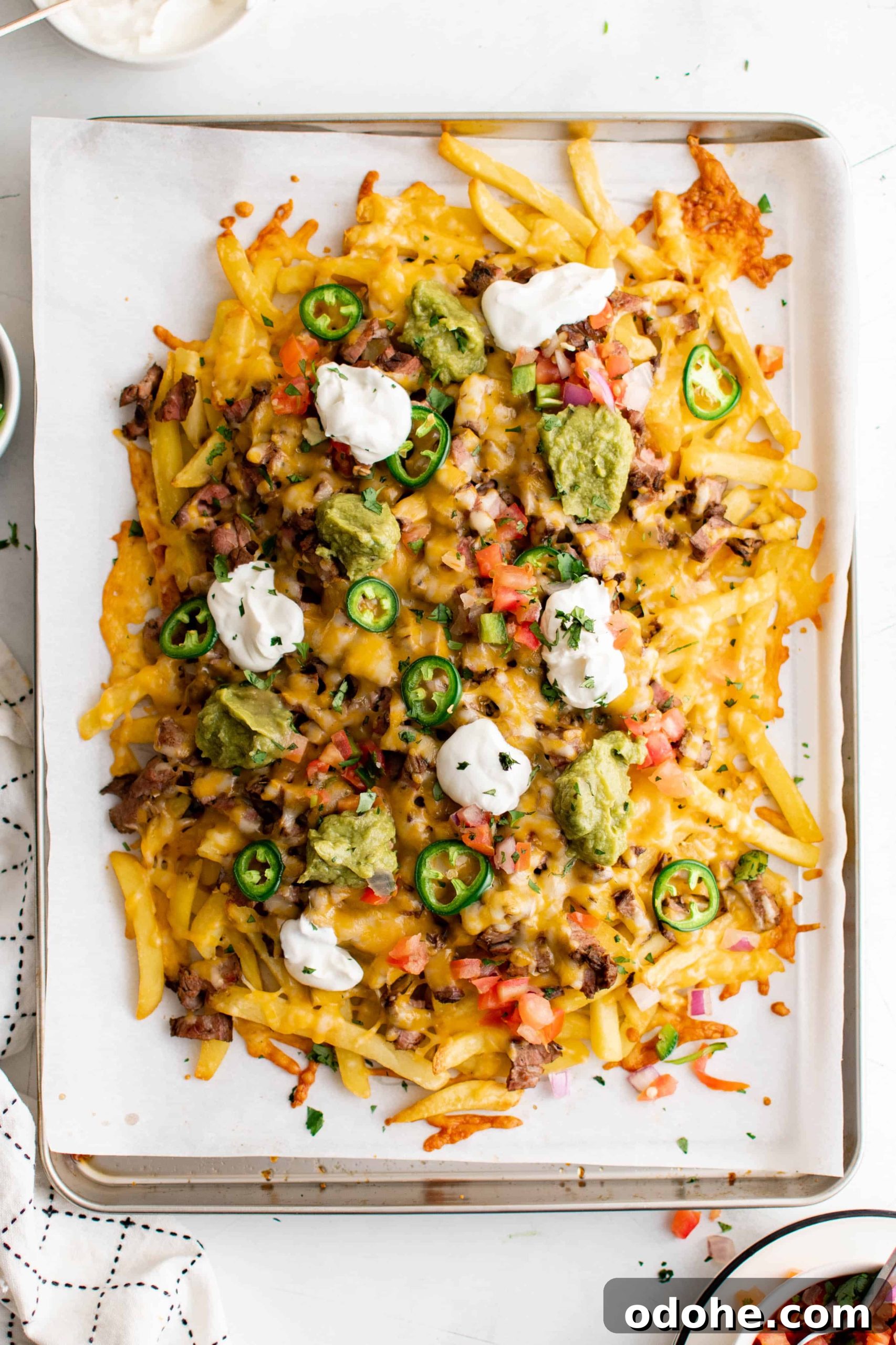 40+ Authentic Mexican Recipes for an Unforgettable Cinco de Mayo 20 Large baking sheet line with parchment paper and filled with french fries smothered with carne asada, cheese, jalapeno, pico de gallo, sour cream, and guacamole.