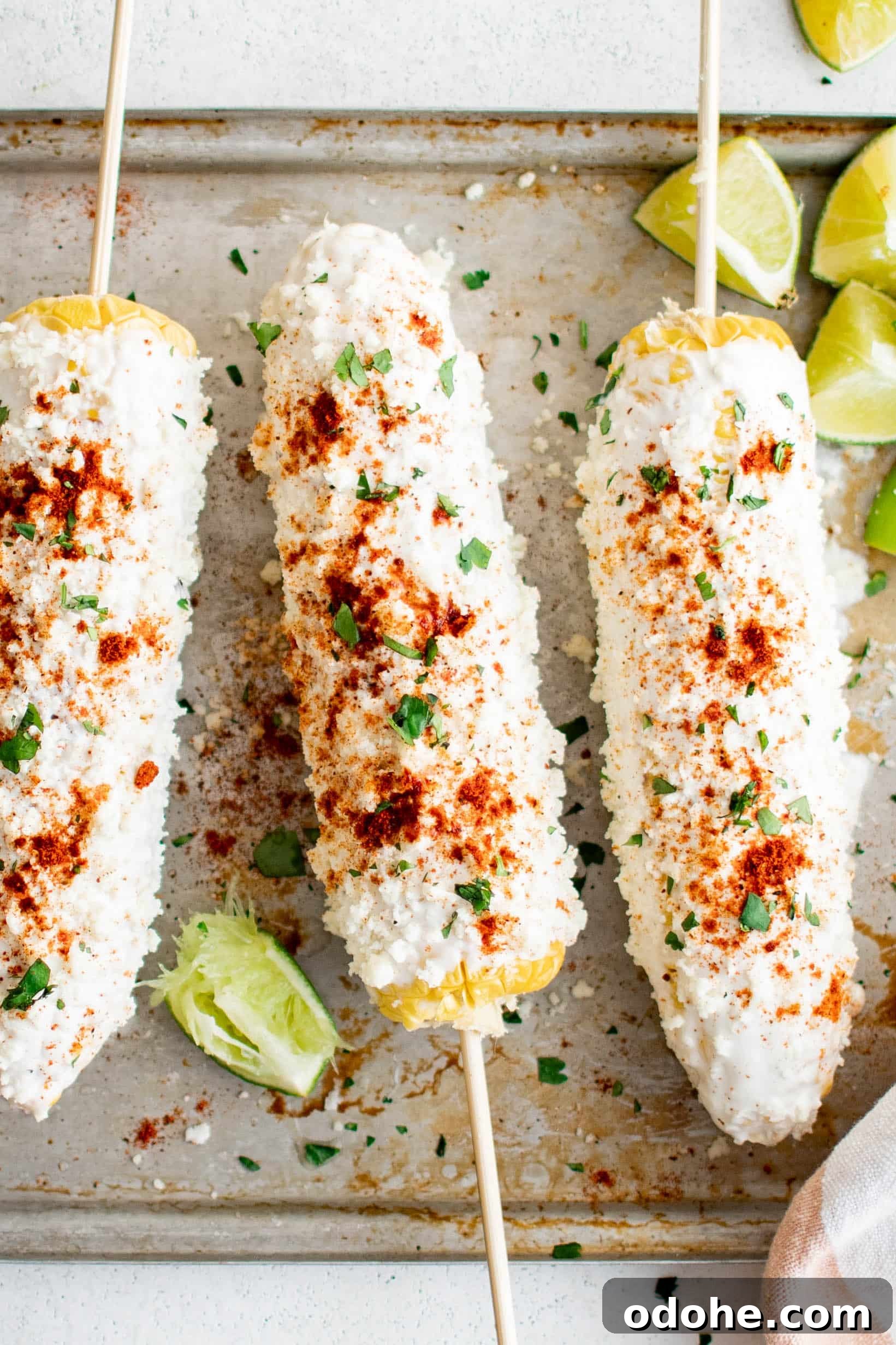 40+ Authentic Mexican Recipes for an Unforgettable Cinco de Mayo 25 Three prepared elote on a baking sheet and garnished with paprika and chili powder, fresh cilantro, and lime wedges.