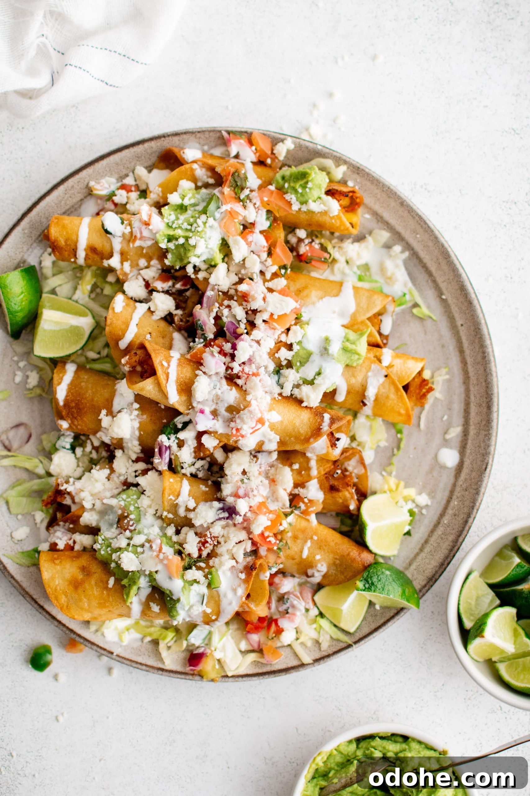 40+ Authentic Mexican Recipes for an Unforgettable Cinco de Mayo 28 Plate filled with deep-fried chicken and potato flautas with shredded iceberg lettuce, crumbled cotija cheese, tomatoes, lime wedges, and guacamole.