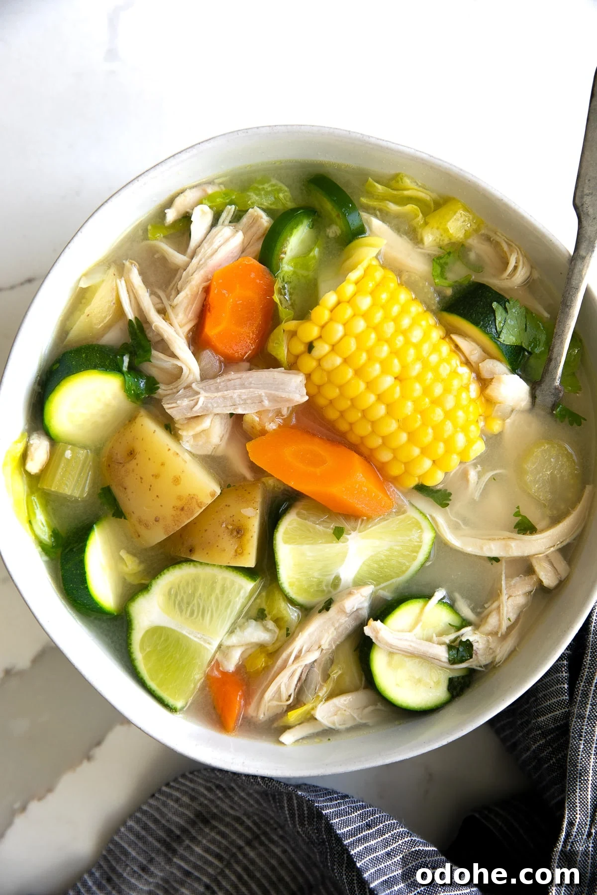 40+ Authentic Mexican Recipes for an Unforgettable Cinco de Mayo 31 Large white shallow bowl filled with caldo de pollo made with chicken, carrots, corn, lime juice, potatoes, and zucchini.