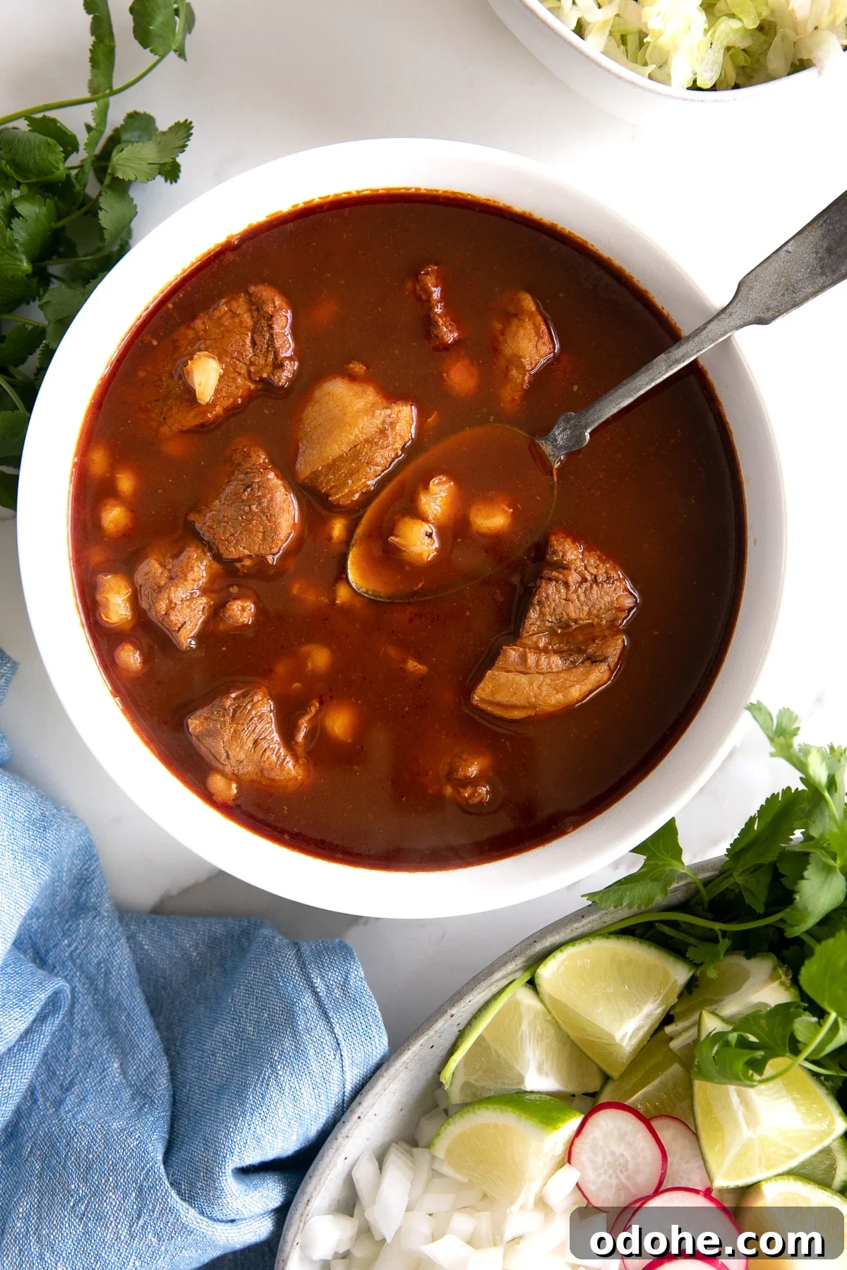 40+ Authentic Mexican Recipes for an Unforgettable Cinco de Mayo 33 Overhead image of a white bowl filled with authentic pozole surrounding by plates filled with optional garnishes.