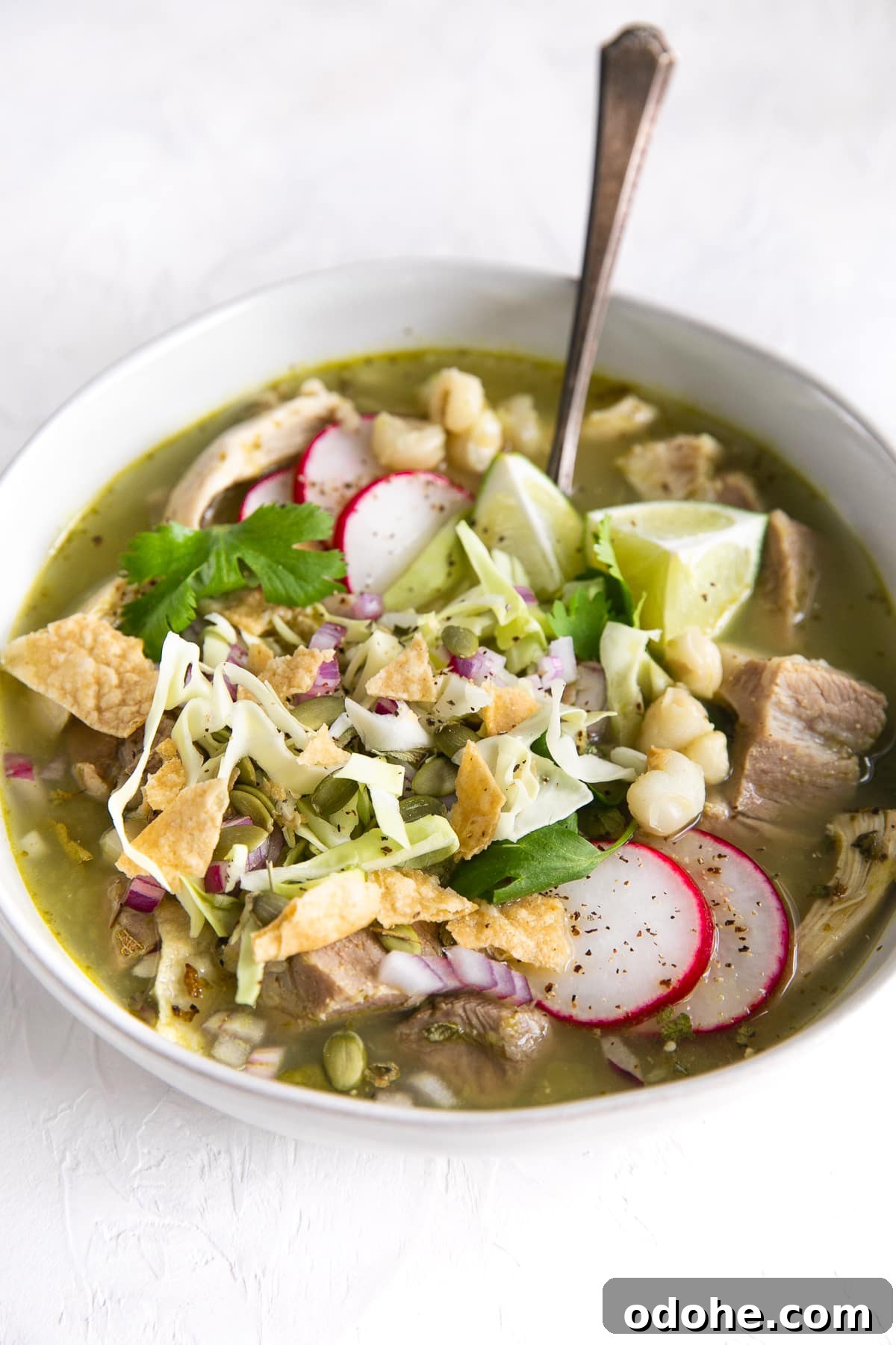 40+ Authentic Mexican Recipes for an Unforgettable Cinco de Mayo 34 White bowl filled with posole verde garnished with shredded cabbage, tortilla chops, cilantro, sliced radish, and lime juice.