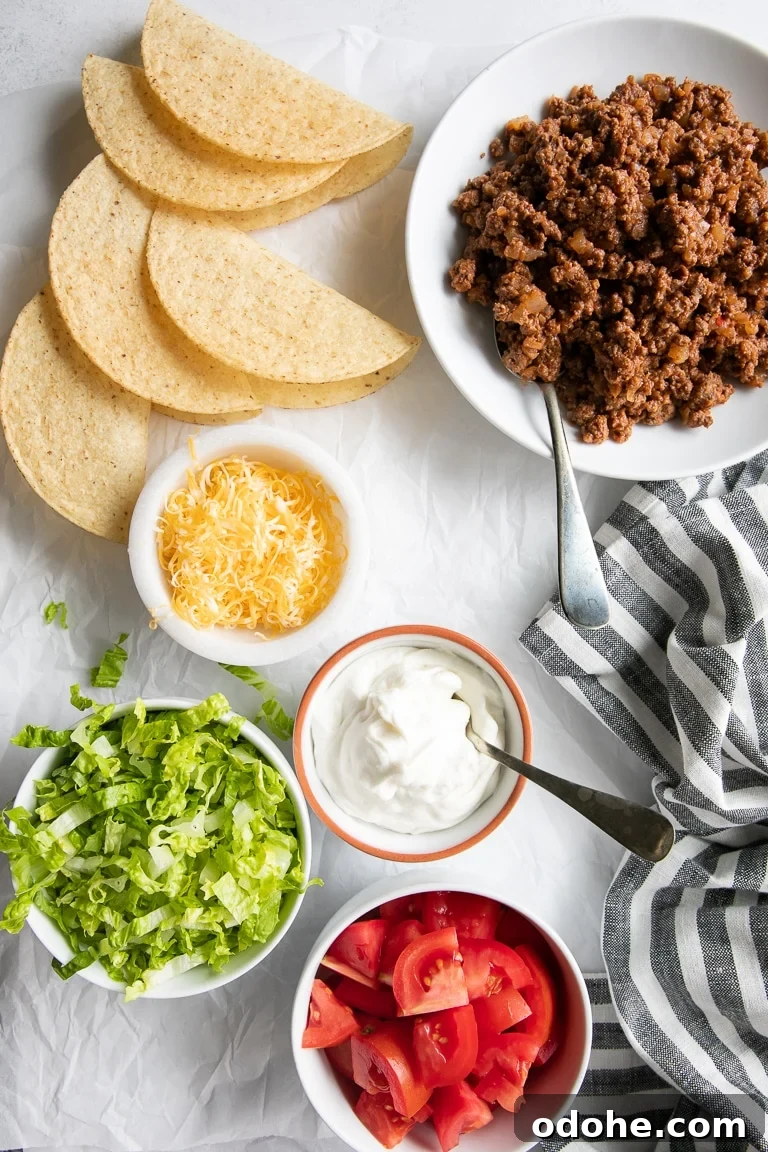 40+ Authentic Mexican Recipes for an Unforgettable Cinco de Mayo 36 Individual bowls filled with seasoned ground beef, shredded cheese, chopped lettuce, sour cream, and diced tomatoes, with hard shell taco shells on the side.