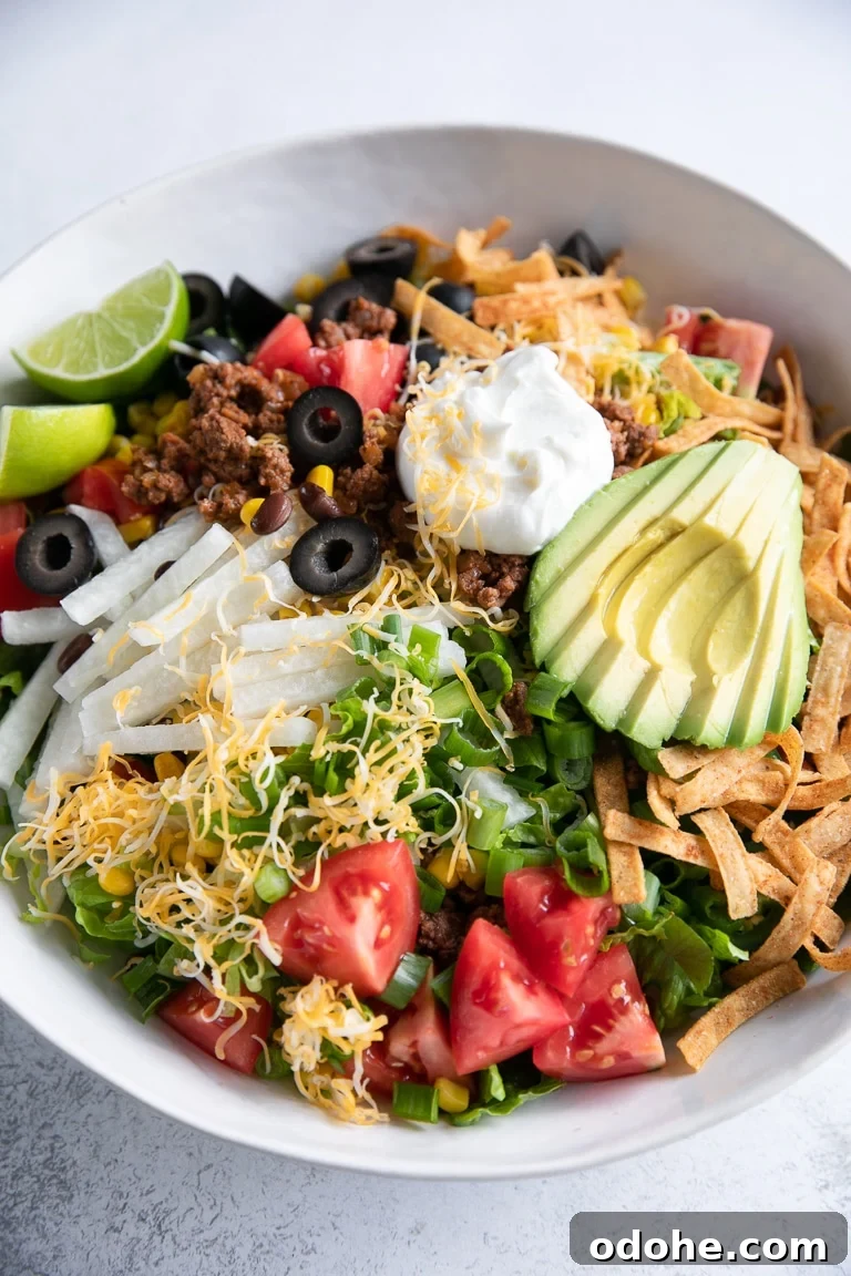 40+ Authentic Mexican Recipes for an Unforgettable Cinco de Mayo 39 Large white bowl filled with beef taco salad topped with shredded cheese, avocado, olives, tomatoes, and sour cream.