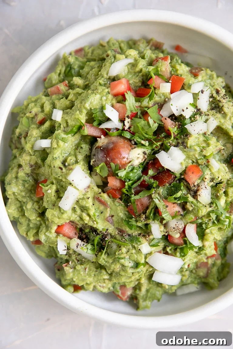 40+ Authentic Mexican Recipes for an Unforgettable Cinco de Mayo 5 Overhead image of guacamole in a white serving bowl garnished with chopped white onion and tomato.